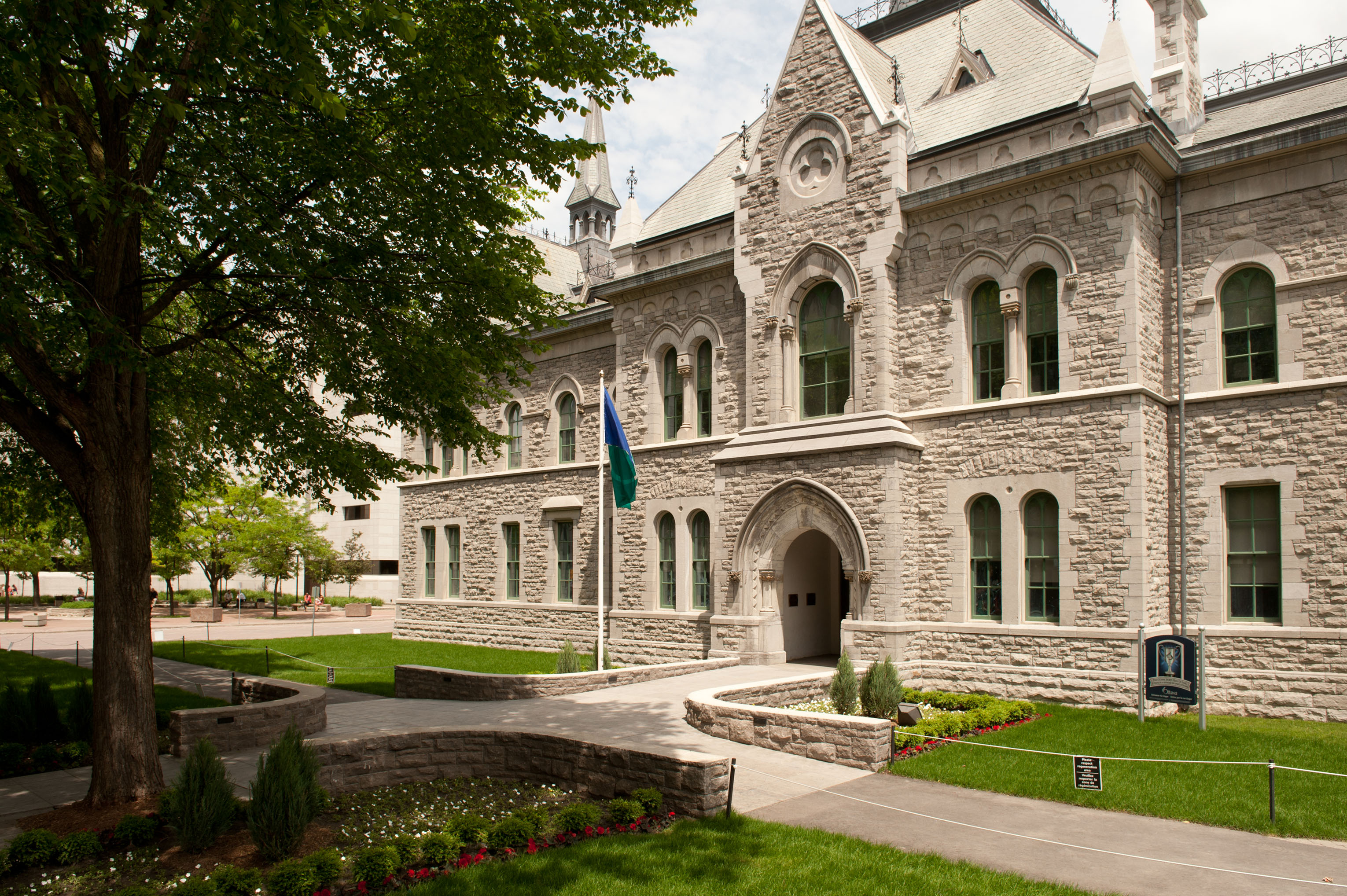 Exterior view of a stone, high-Victorian style building and a large tree.